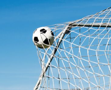 Soccer ball moves through the air and hits the goal. It's placed perfectly in the upper corner. Blue sky as background.