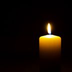 One yellow candle flame burning in darkness on black background with copy space for text.