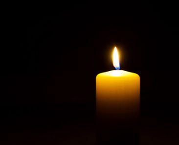 One yellow candle flame burning in darkness on black background with copy space for text.